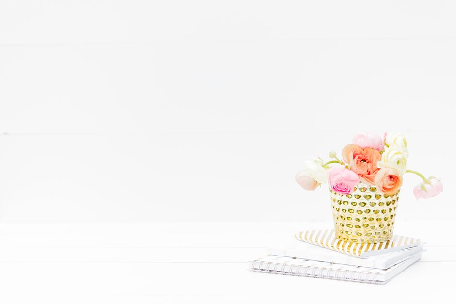 Beautiful bouquet of flowers in a golden vase atop stacked notebooks, perfect for creative workspace decor.